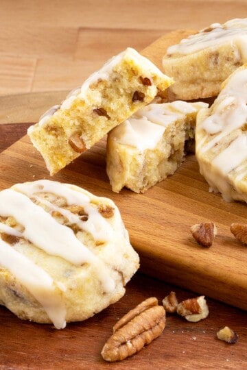 Fig pecan shortbread cookies with honey orange glaze sitting on a board with one cookie broken in half to show texture.
