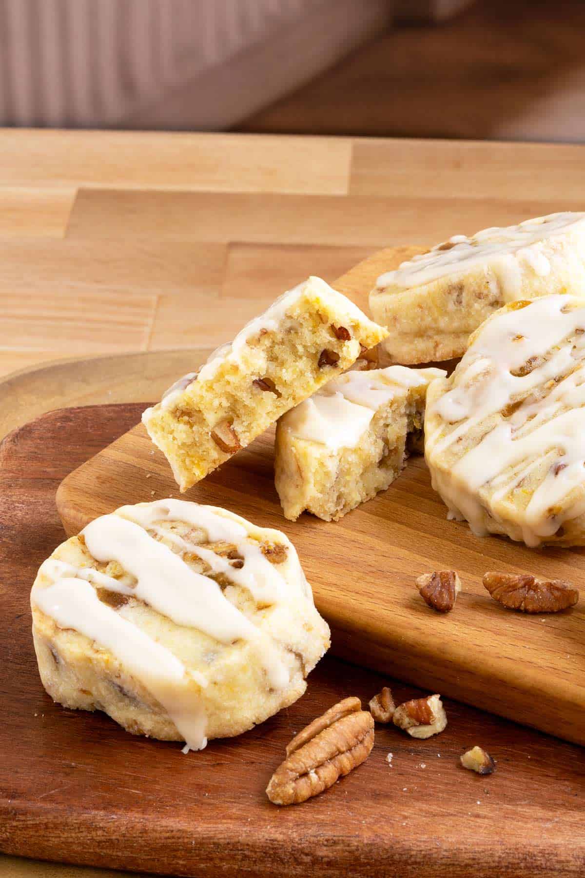 Fig pecan shortbread cookies with honey orange glaze sitting on a board with one cookie broken in half to show texture and size.