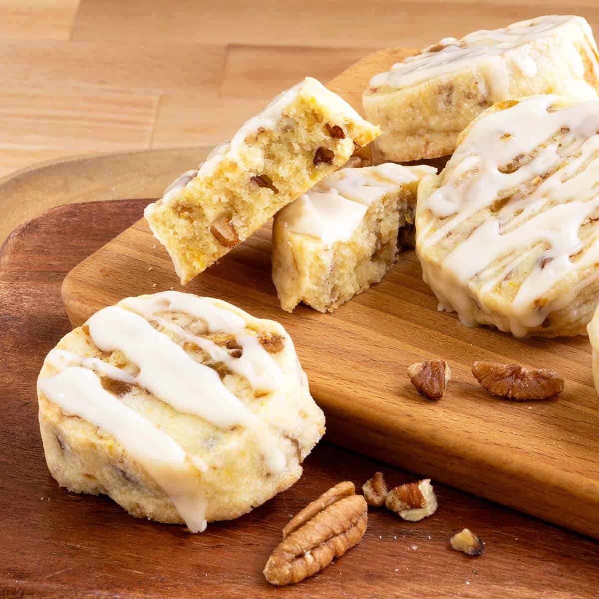 Fig pecan shortbread cookies with honey orange glaze sitting on a board with one cookie broken in half to show texture.