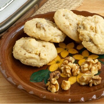 Glazed maple walnut cookies on a small plate with some walnut pieces.