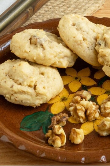 Glazed maple walnut cookies on a small plate with some walnut pieces.