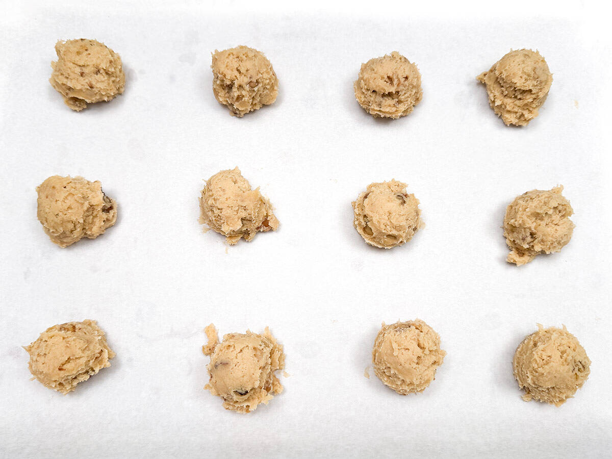 Scooped glazed maple walnut cookies on a parchment lined cookie sheet pan.