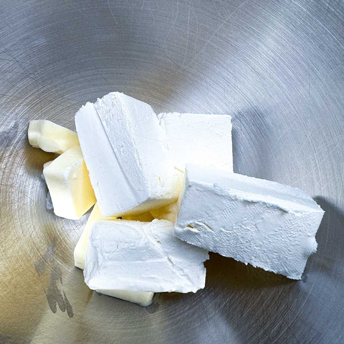 Cubed butter and blocks of cream cheese in a mixer bowl.
