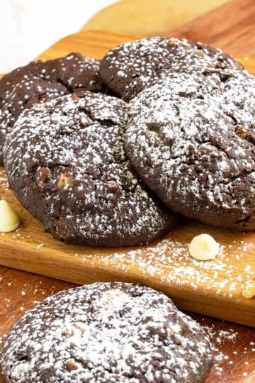 Chocolate cookies with white chocolate and caramel arranged on a wooden board with powdered sugar sprinkled on top of the cookies.