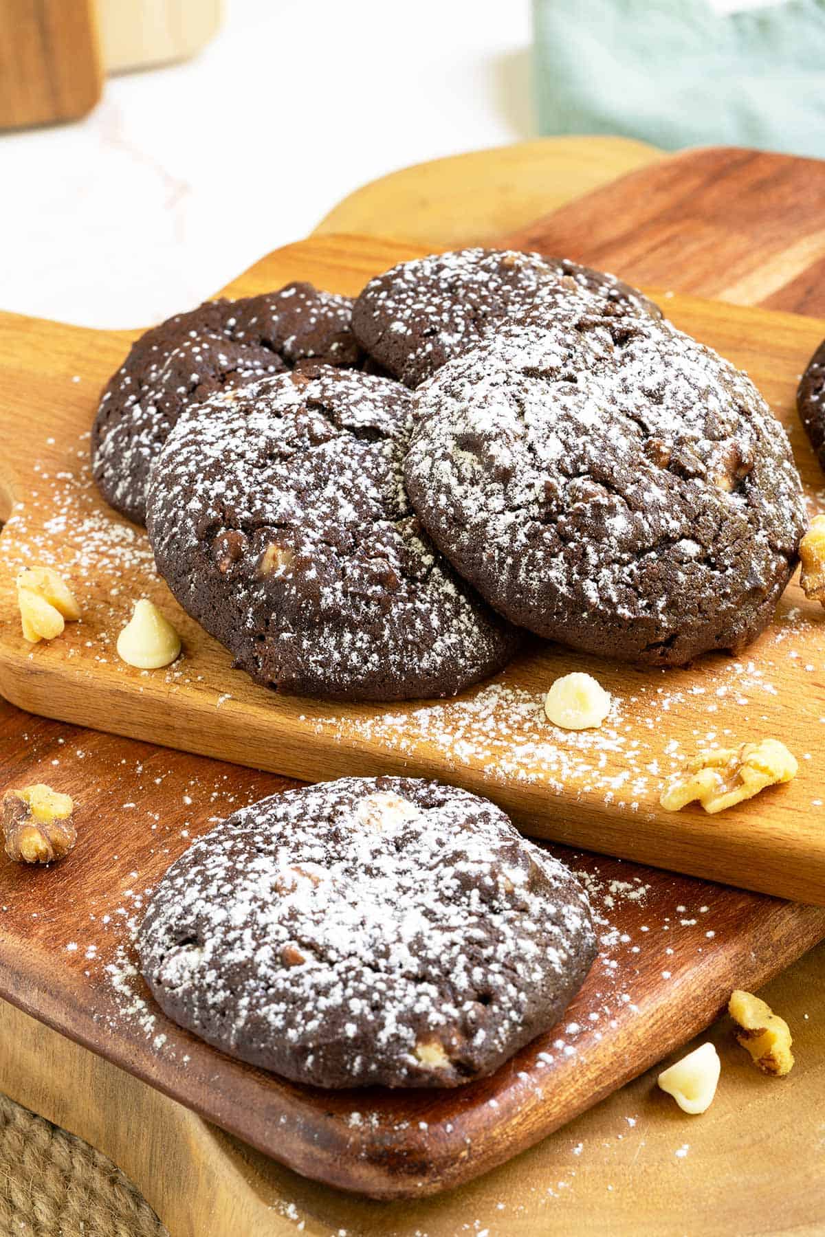 Chocolate cookies with white chocolate and caramel arranged on a wooden board with white chocolate chips and walnuts spread around.