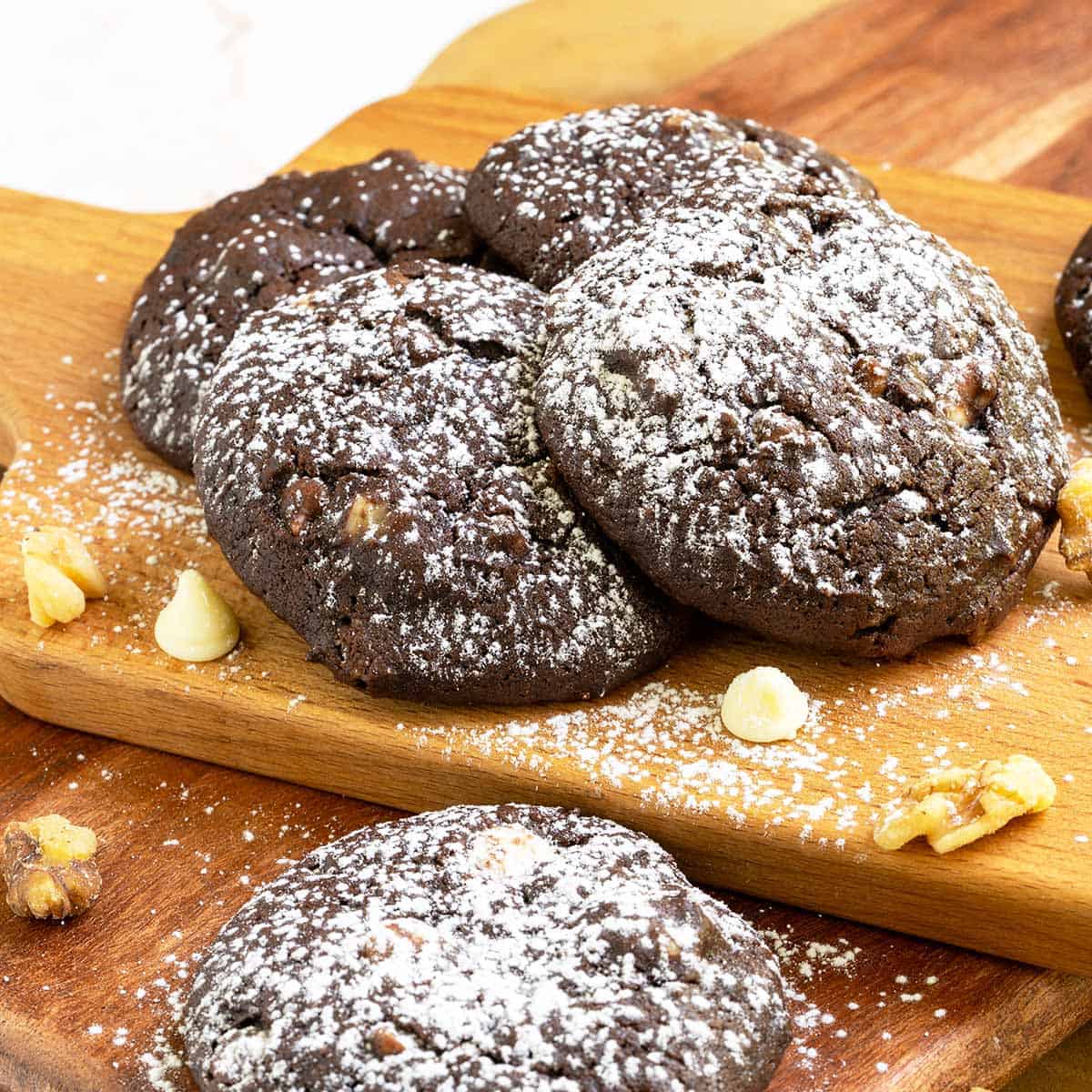 Chocolate cookies with white chocolate and caramel arranged on a wooden board with powdered sugar sprinkled on top of the cookies.
