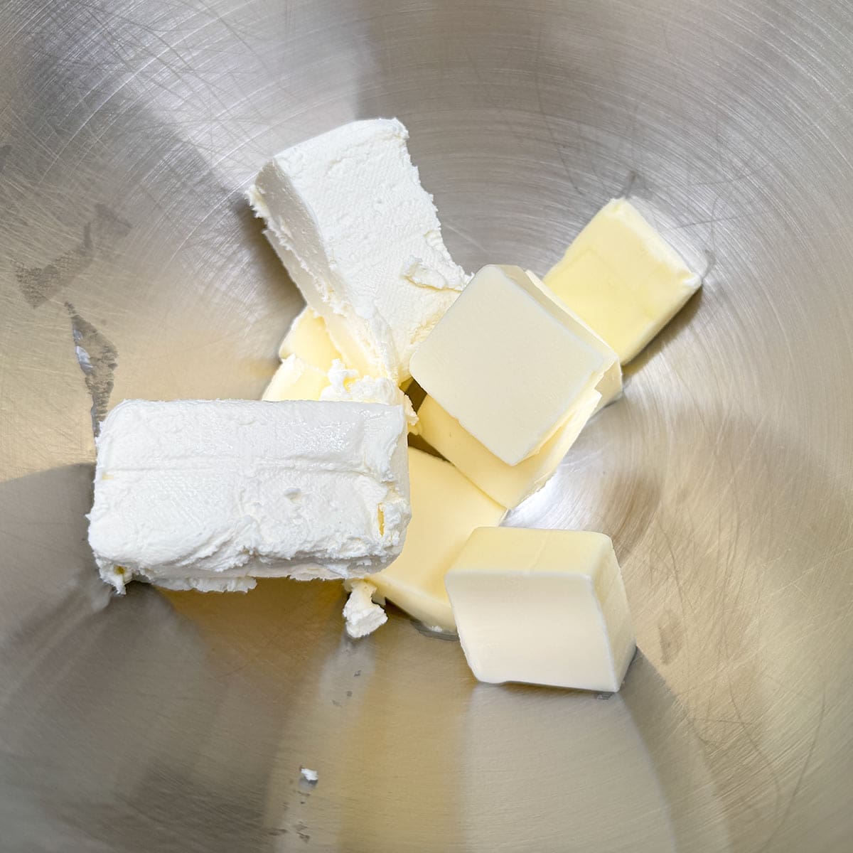 Cubed butter and blocks of cream cheese in a mixer bowl.