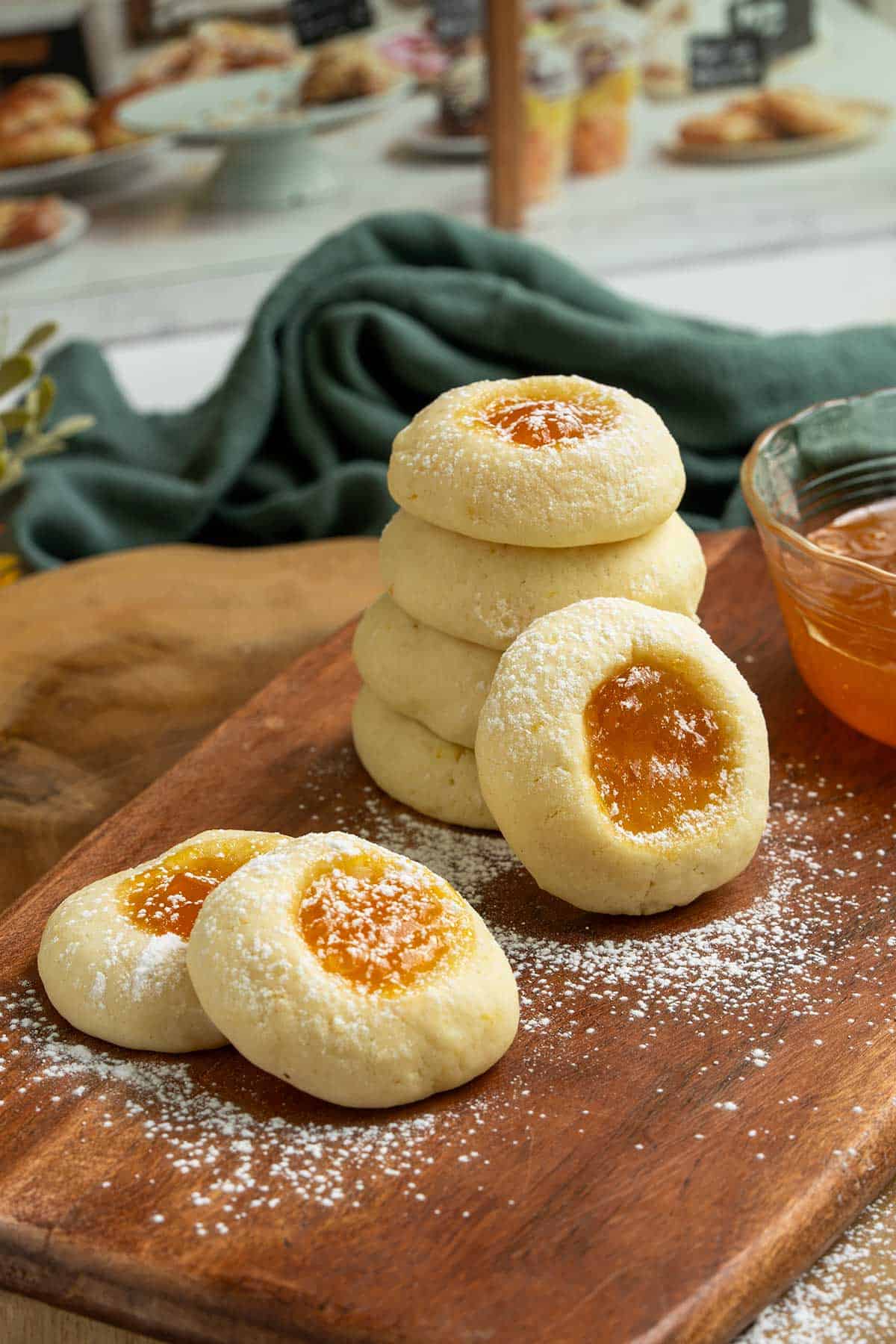 Apricot Cream Cheese Cookies stacked with powdered sugar sprinkled on top and a small bowl of apricot preserves right beside the cookies.