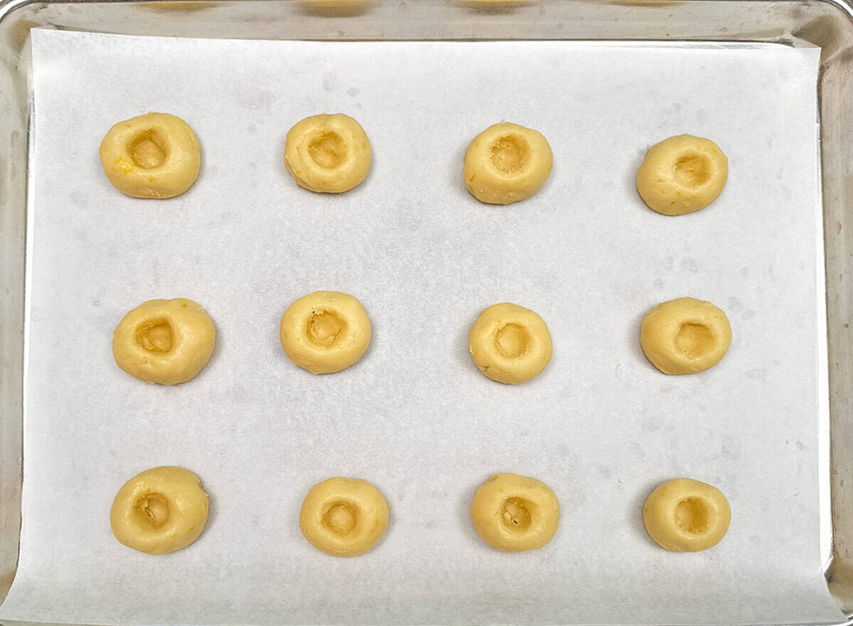 Cookie balls that have the holes added on a parchment-lined cookie sheet pan.
