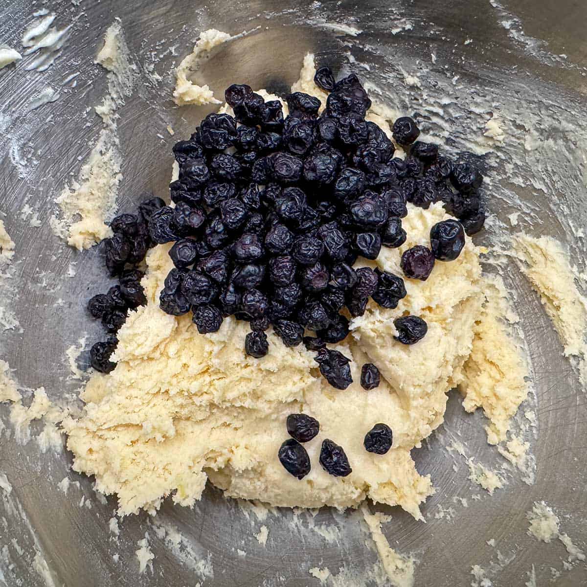 A bowl of cookie dough getting dried blueberries to be mixed in.