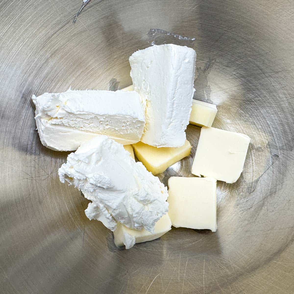 Cubed butter and blocks of cream cheese in a mixer bowl.