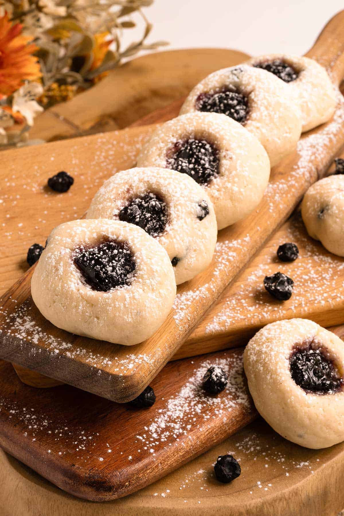 Blueberry cream cheese thumbprint cookies lined up on a stack of cutting boards.