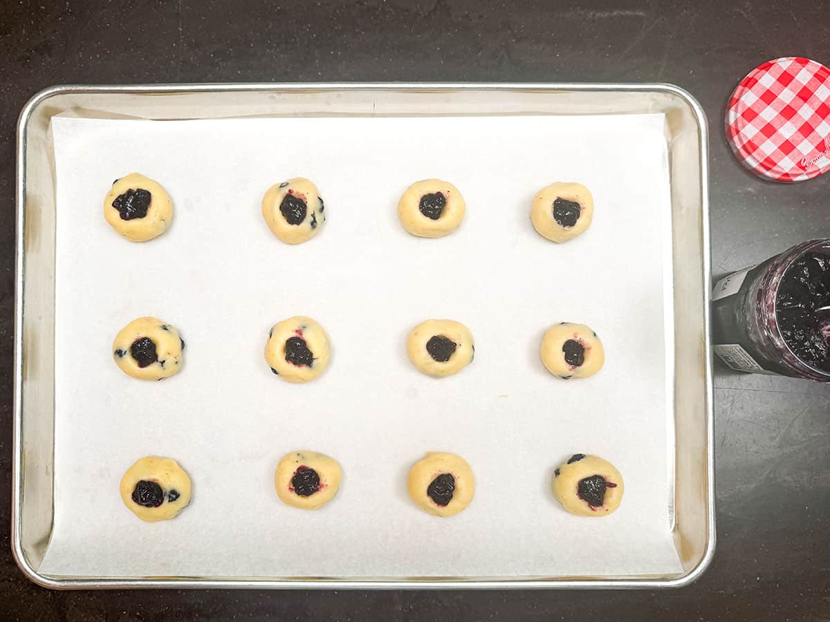 A cookie pan with twelve blueberry cream cheese thumbprint cookies filled and ready for the oven.