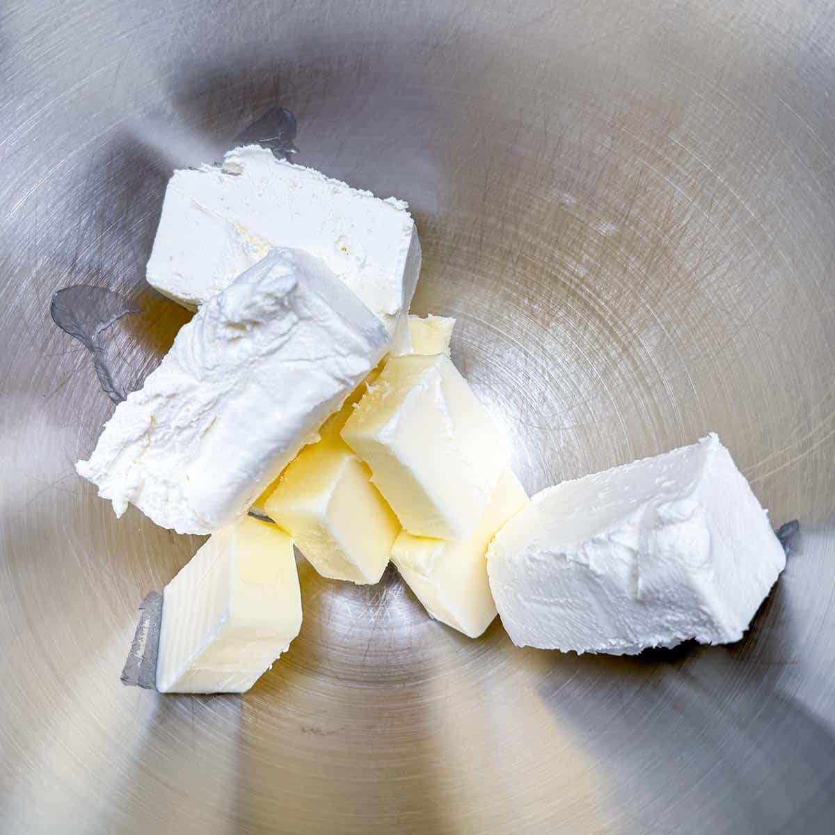 Cubed butter and small blocks of cream cheese in a mixer bowl.