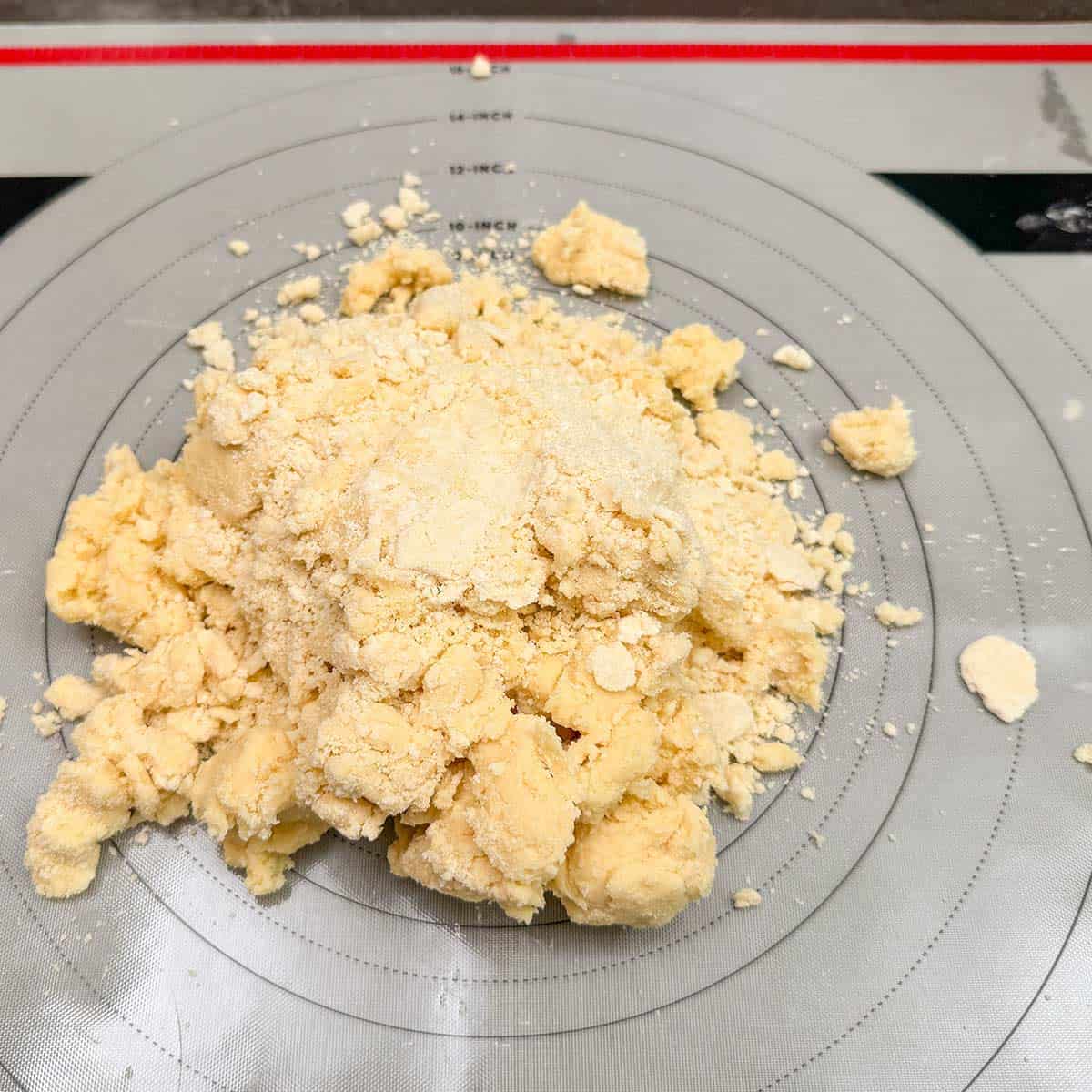 The partially mixed cookie dough placed on a pastry mat to be hand mixed by kneaded the dough into a log shape.