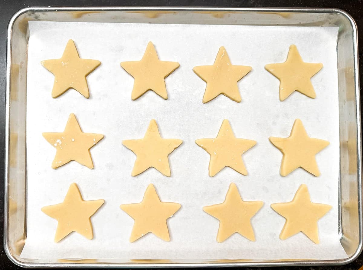 Twelve cutout stars on a parchment lined cookie sheet pan ready for the oven.