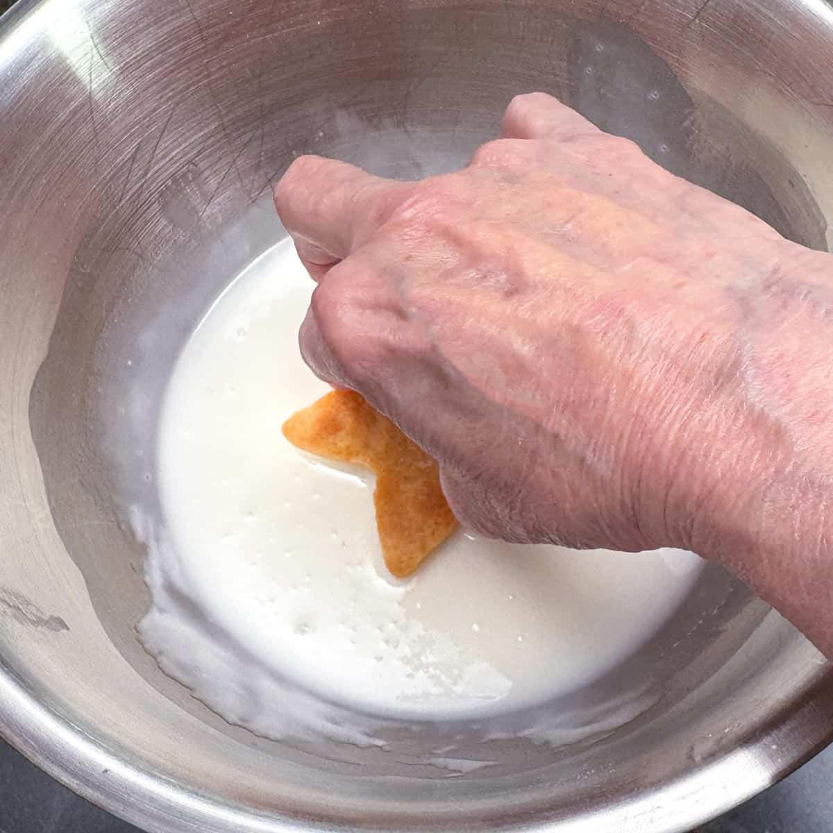 Dipping the top of a baked cookie to add the almond glaze.