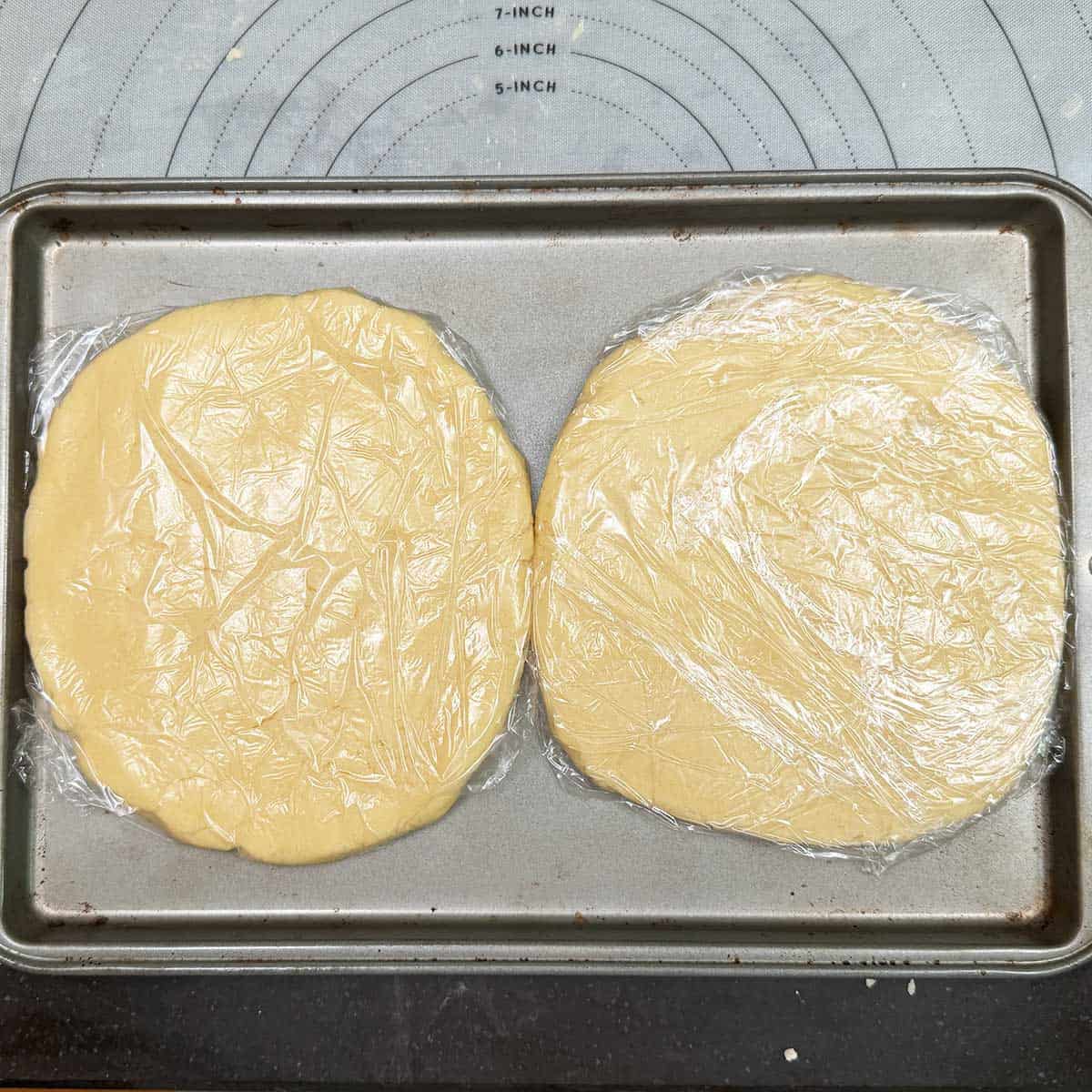 Two plastic wrapped disked of cookie dough getting ready to go into the fridge.