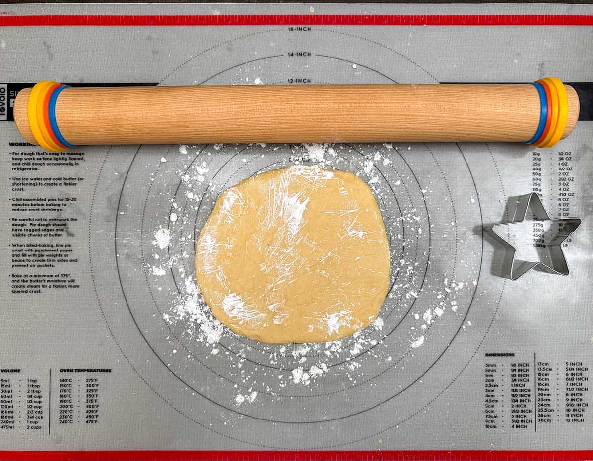 Chilled cookie dough disk with a rolling pin and star shaped cookie cutter on a pastry mat.
