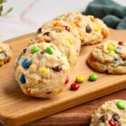 Completed Peanut Butter M&M and Reese's Pieces Cookies on a board with pieces of candy laying around..