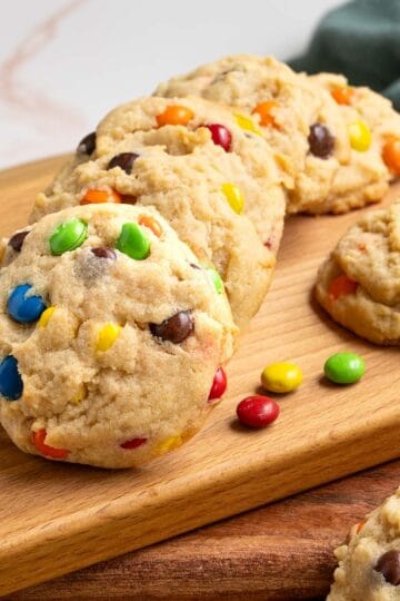 Completed Peanut Butter M&M and Reese's Pieces Cookies on a board with pieces of candy laying around..