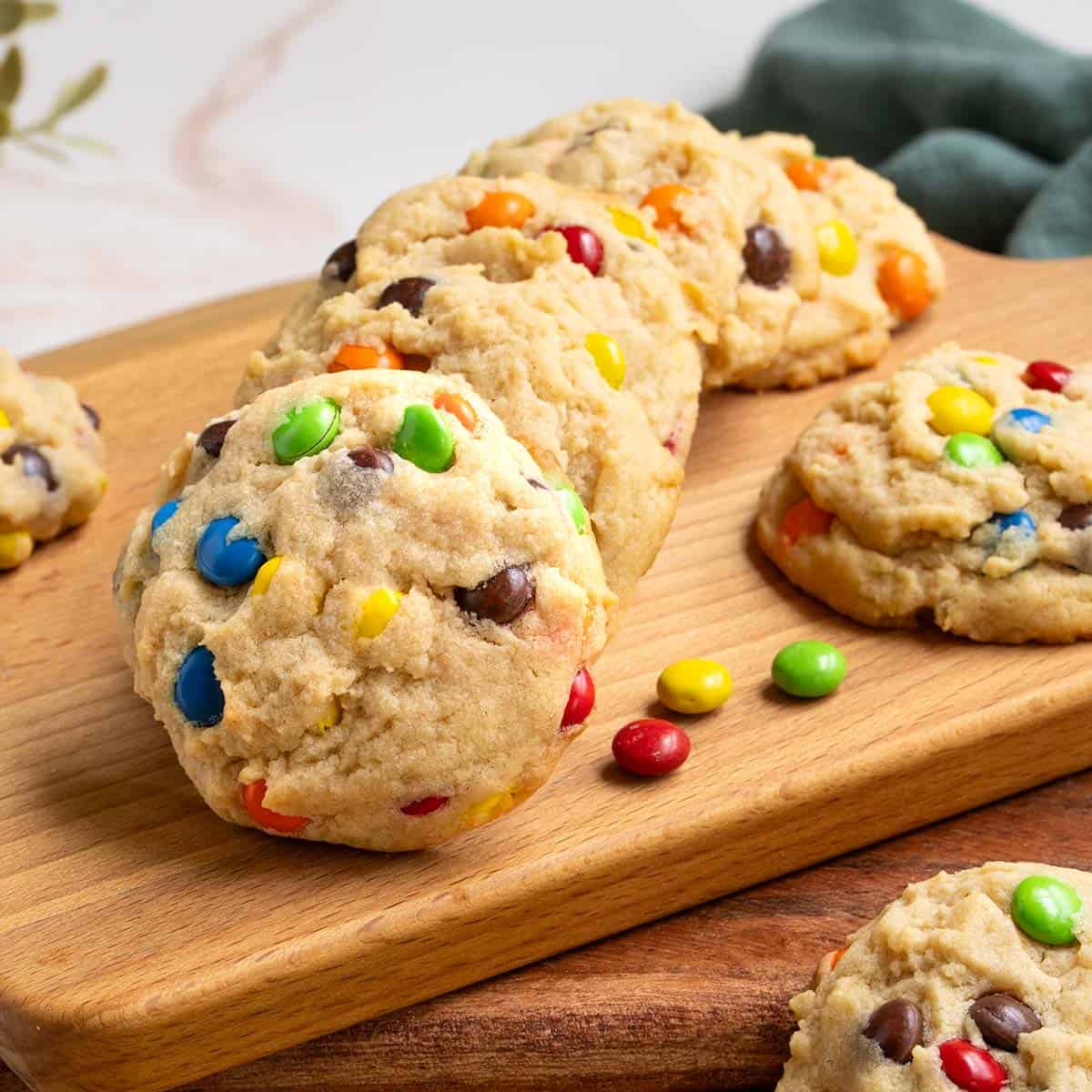Completed Peanut Butter M&M and Reese's Pieces Cookies on a board with pieces of candy laying around..