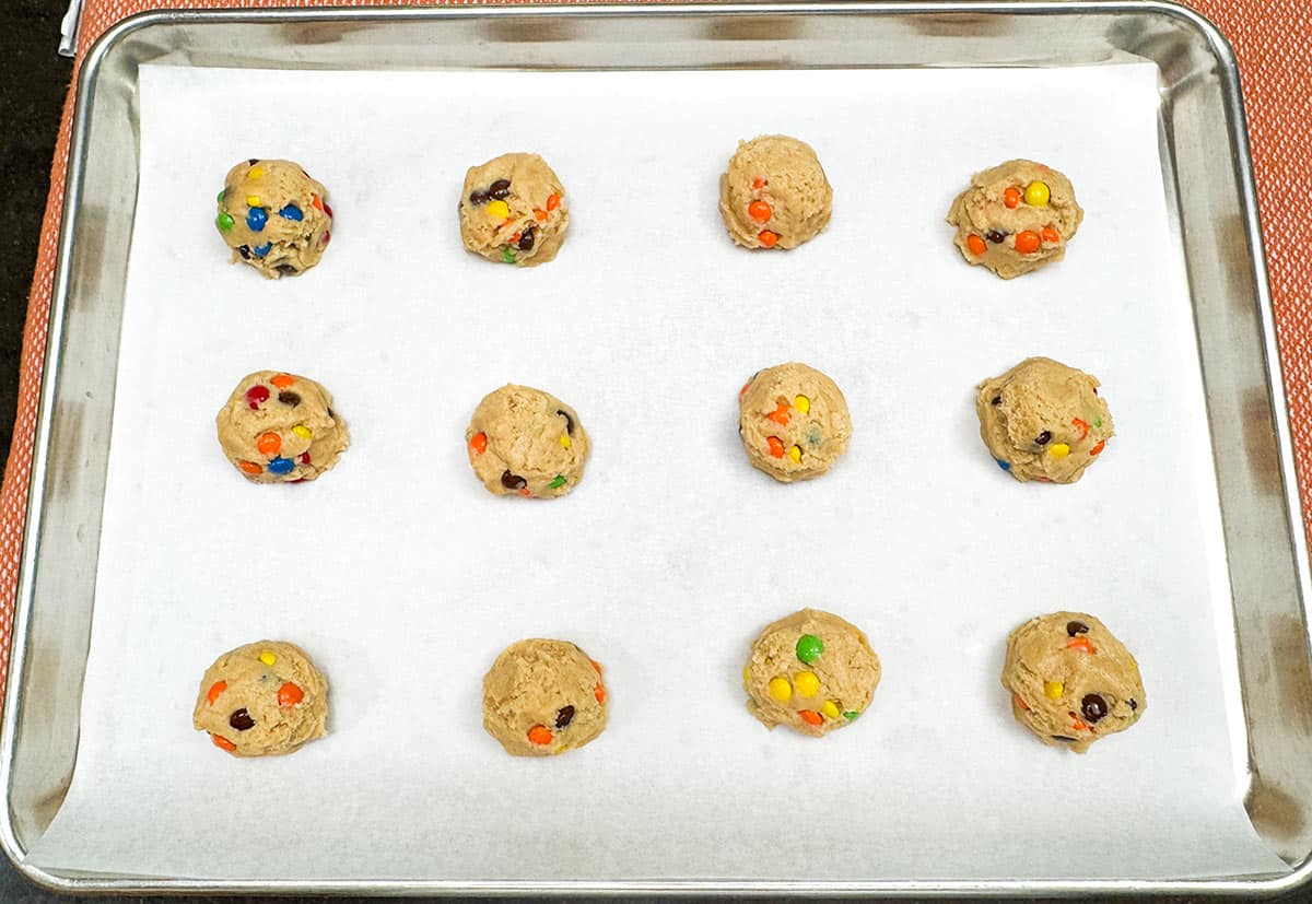 Twelve scoops of cookie dough on a parchment lined cookies sheet pan ready for the oven.