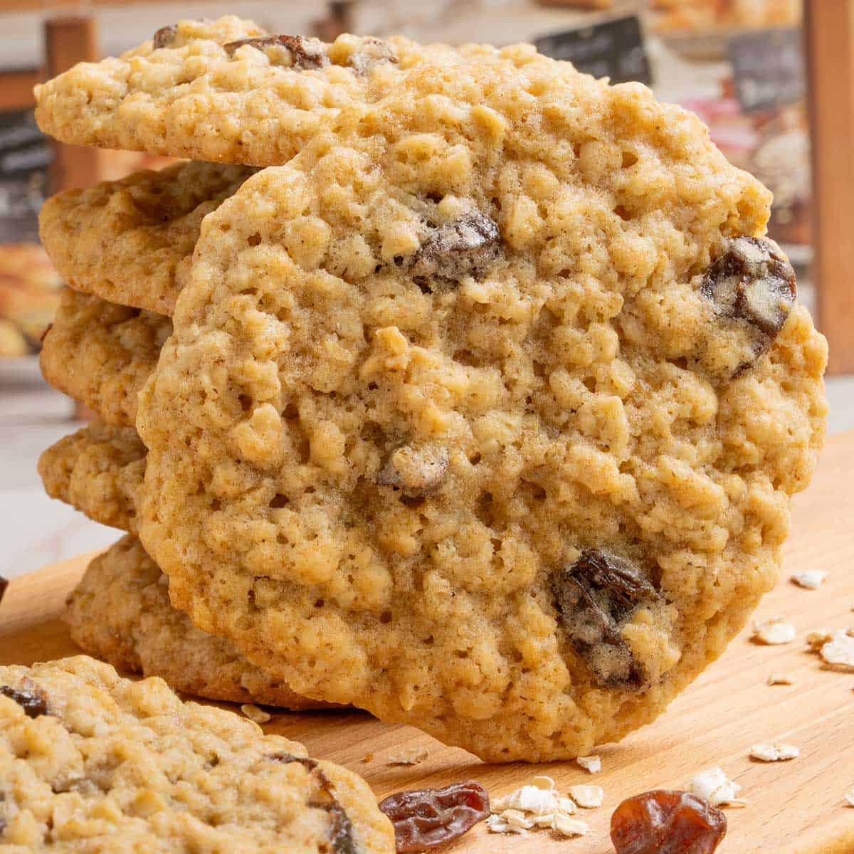 A stack and front view of Spiced Oatmeal Raisin Cookies on a board with oats and raisins around the cookies.