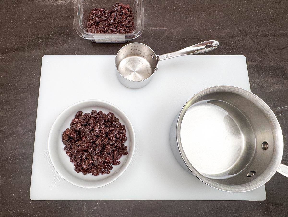 A bowl of raisins and a pot of very hot water that will be used to soak and plump the raisins.