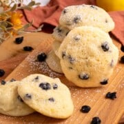 Blueberry Lemon with Mascarpone Cookies are stacked on a wooden board with dried blueberries laying around.