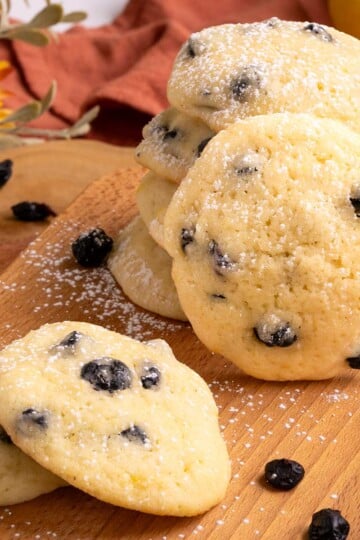 Blueberry Lemon with Mascarpone Cookies are stacked on a wooden board with dried blueberries laying around.