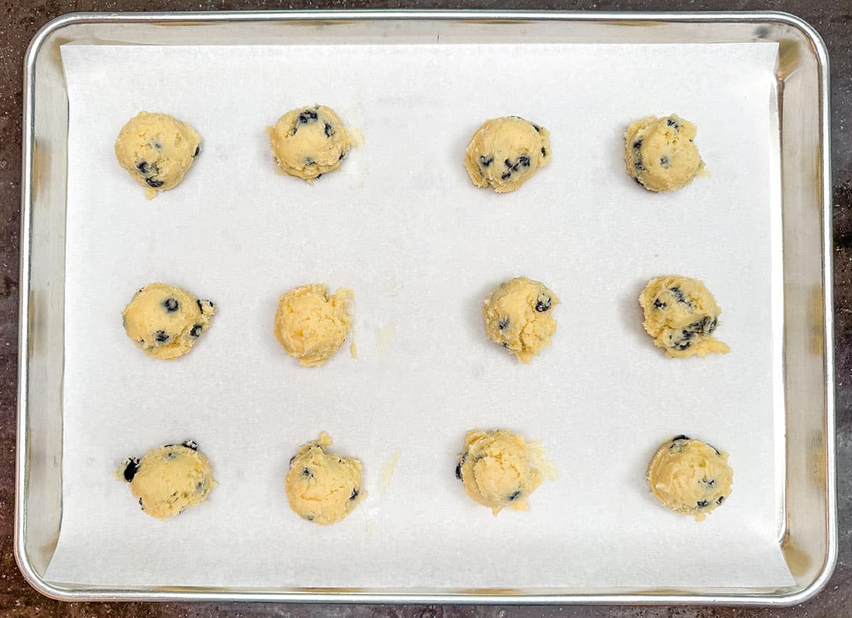 Scooped cookie dough on a parchment-lined cookie sheet pan.