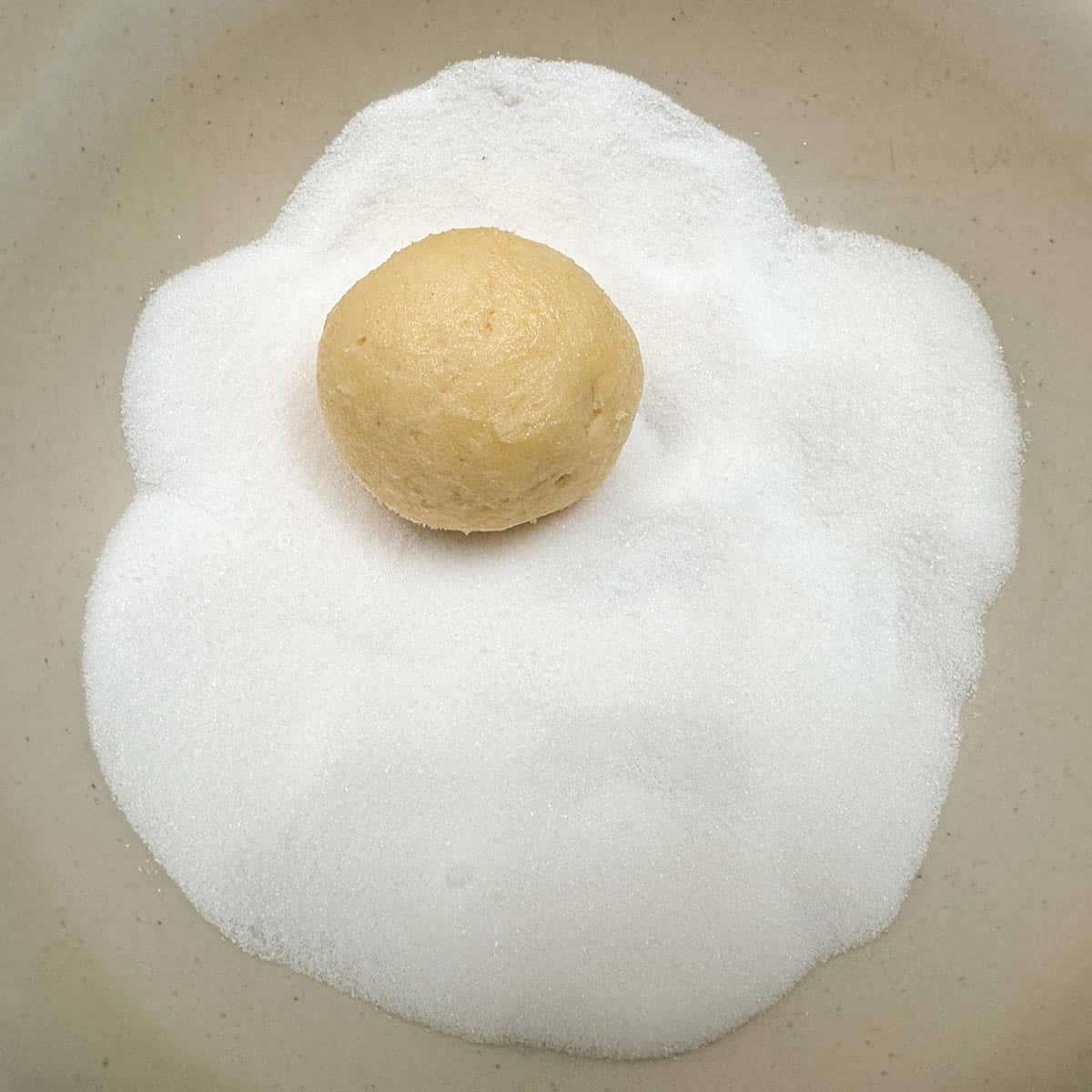 Cookie ball in the bowl of sugar getting ready to be coated.