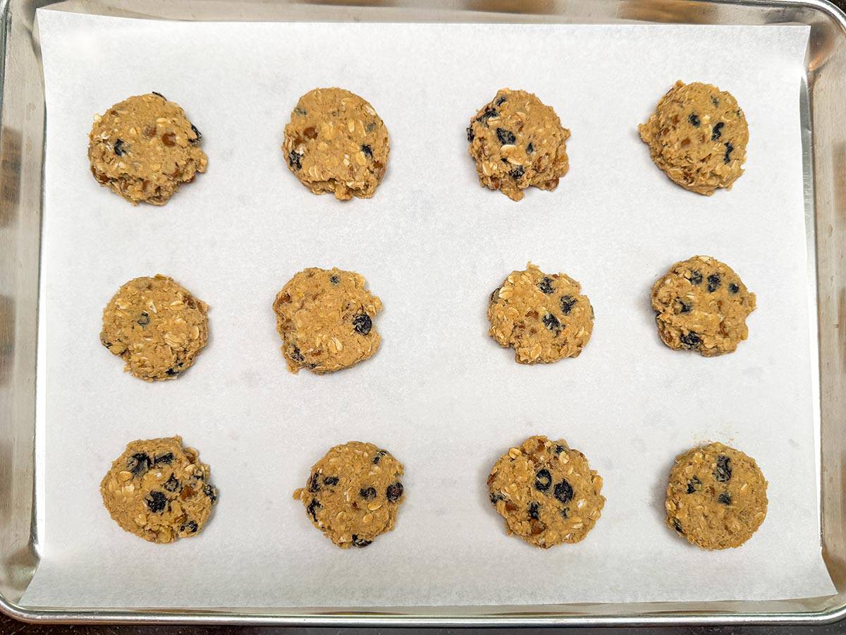 Twelve half flattened scooped cookie dough on a parchment-lined sheet pan.