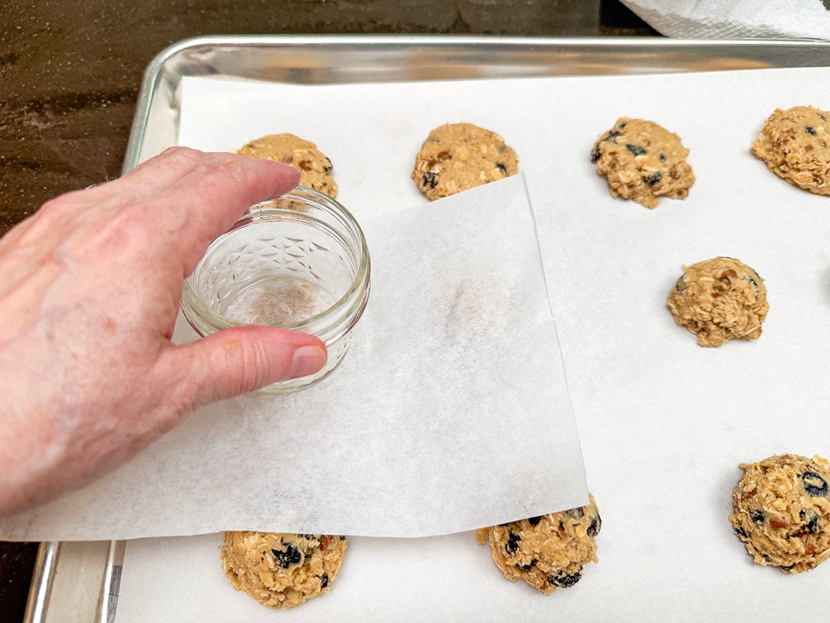 A small square of parchment paper passed over a scooped cookie dough with a glass to press down on top to half flatten the scoop.