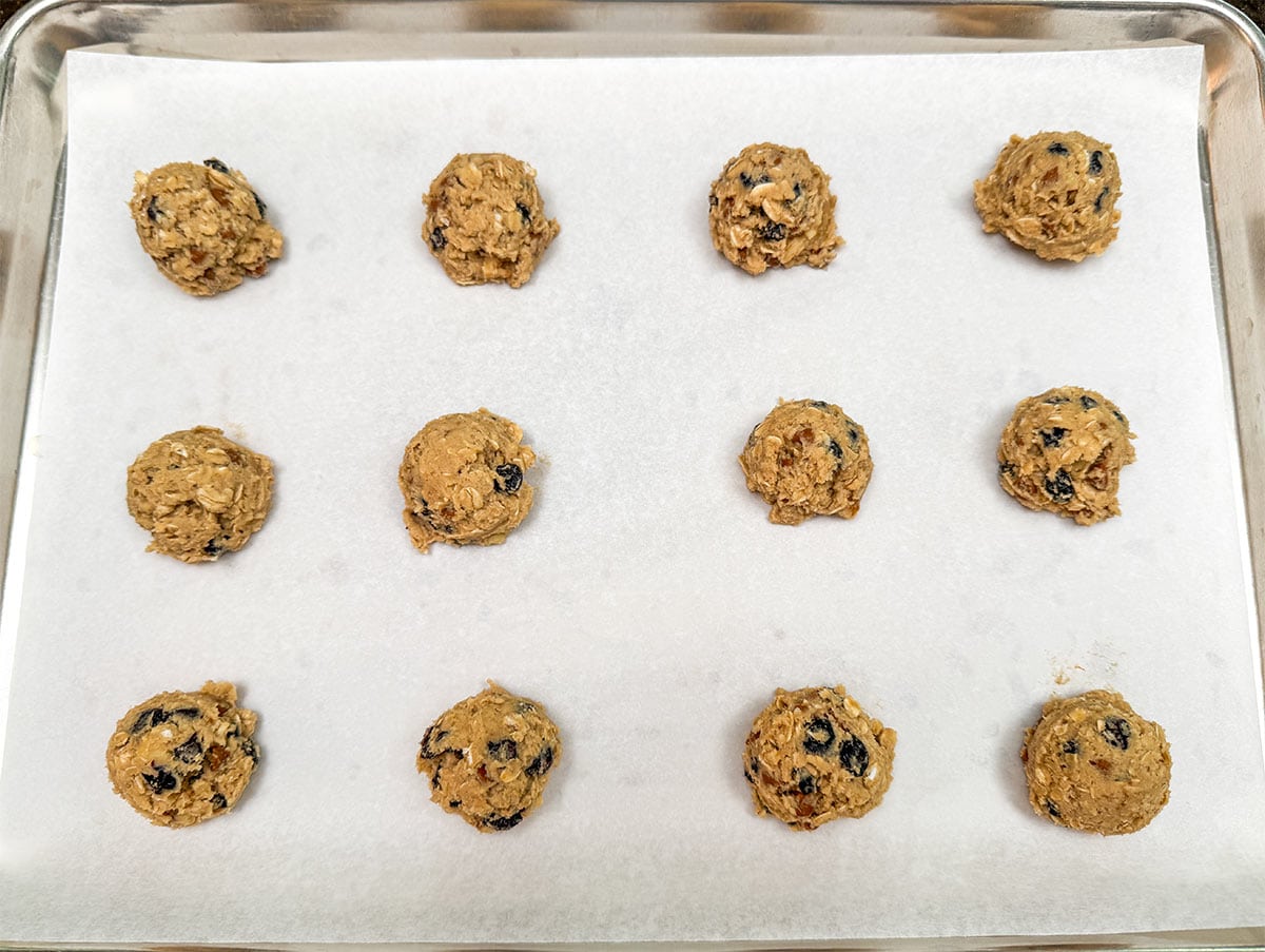 Twelve scooped cookie dough on a parchment-lined sheet pan.