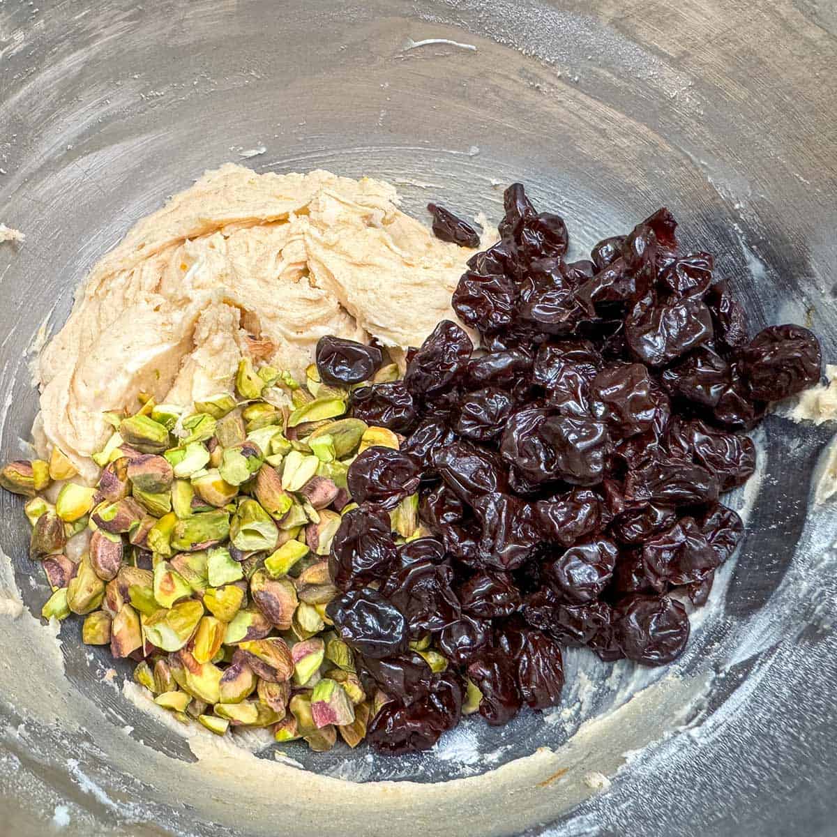 Adding the rough chopped pistachios and dried cherries to the cookies dough in the mixing bowl.