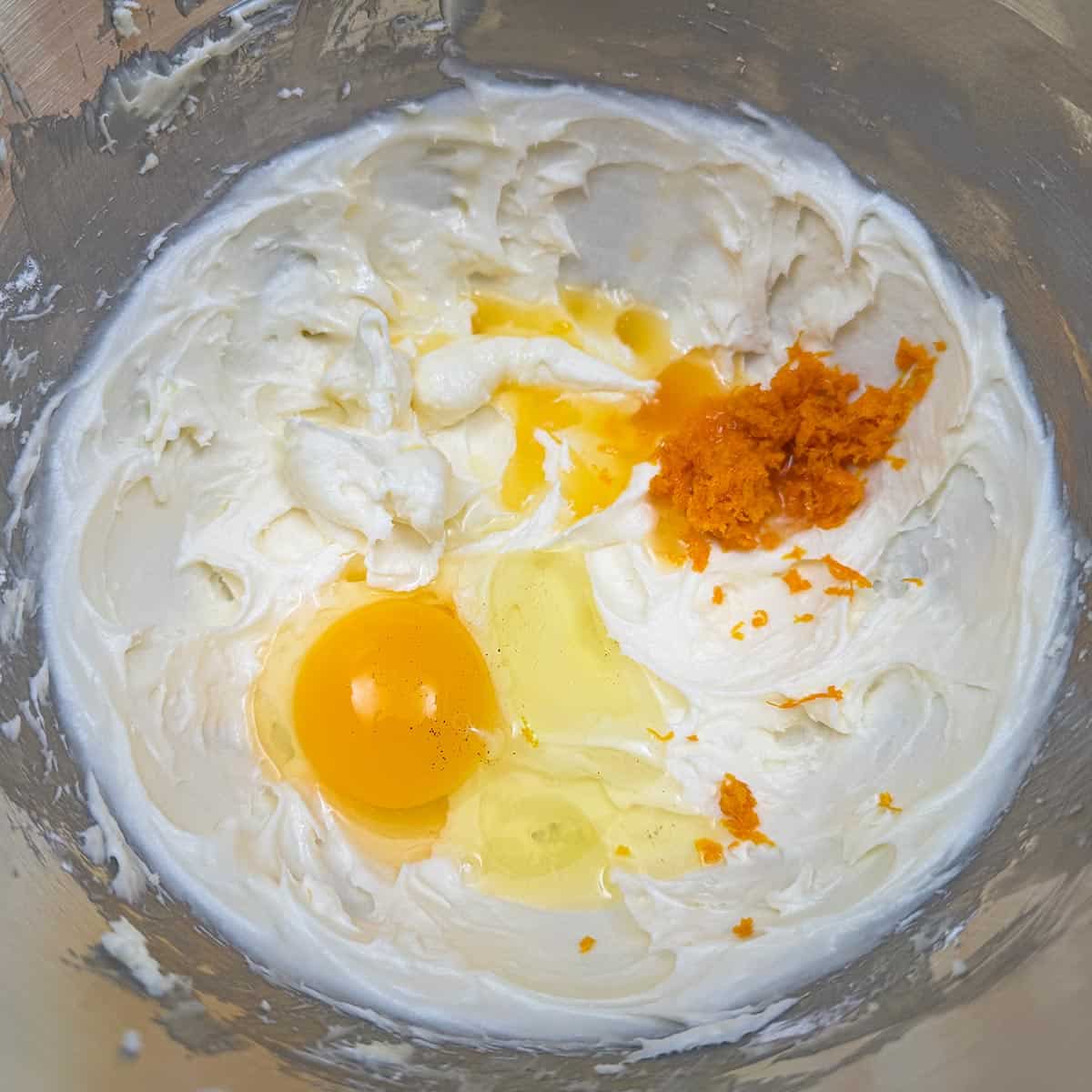 Adding the egg, orange zest and orange juice to the sugar-butter mixture in a mixer bowl.