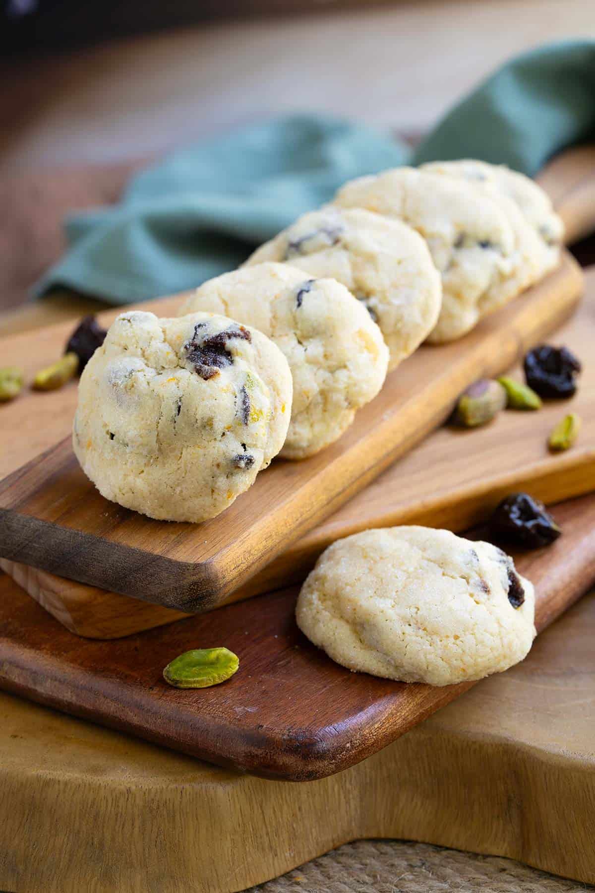 Cherry Orange with Pistachio Cookies lined up on a wooden board. The orange zest and the cherries show through the baked cookies.