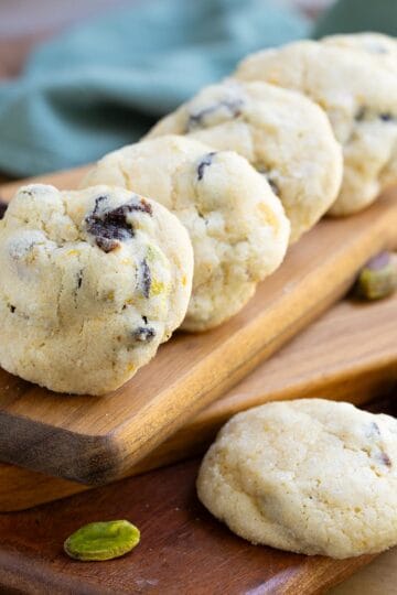 Cherry Orange with Pistachio Cookies lined up on a wooden board. The cherries and orange zest show through.