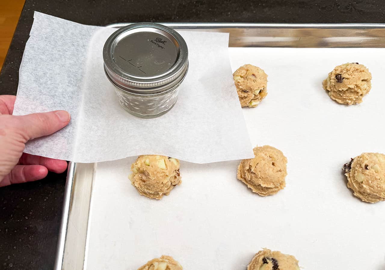 Placing a small piece of parchment paper over a scooped cookie dough and pressing down on the top to flatten the dome a little.