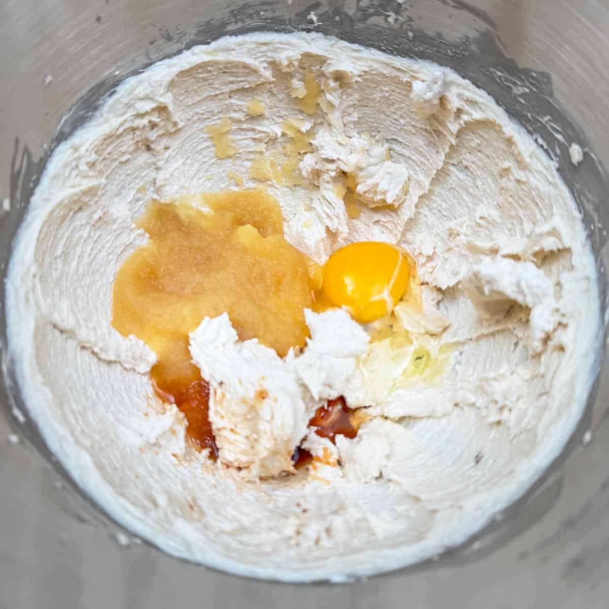 Adding the applesauce, egg, and vanilla extract to the butter-sugar mixture in the mixer bowl.
