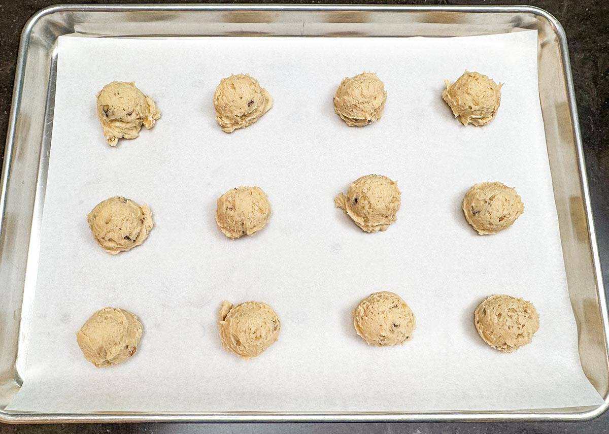 Scooped applesauce and walnut cookie dough onto a sheet pan lined with parchment paper.