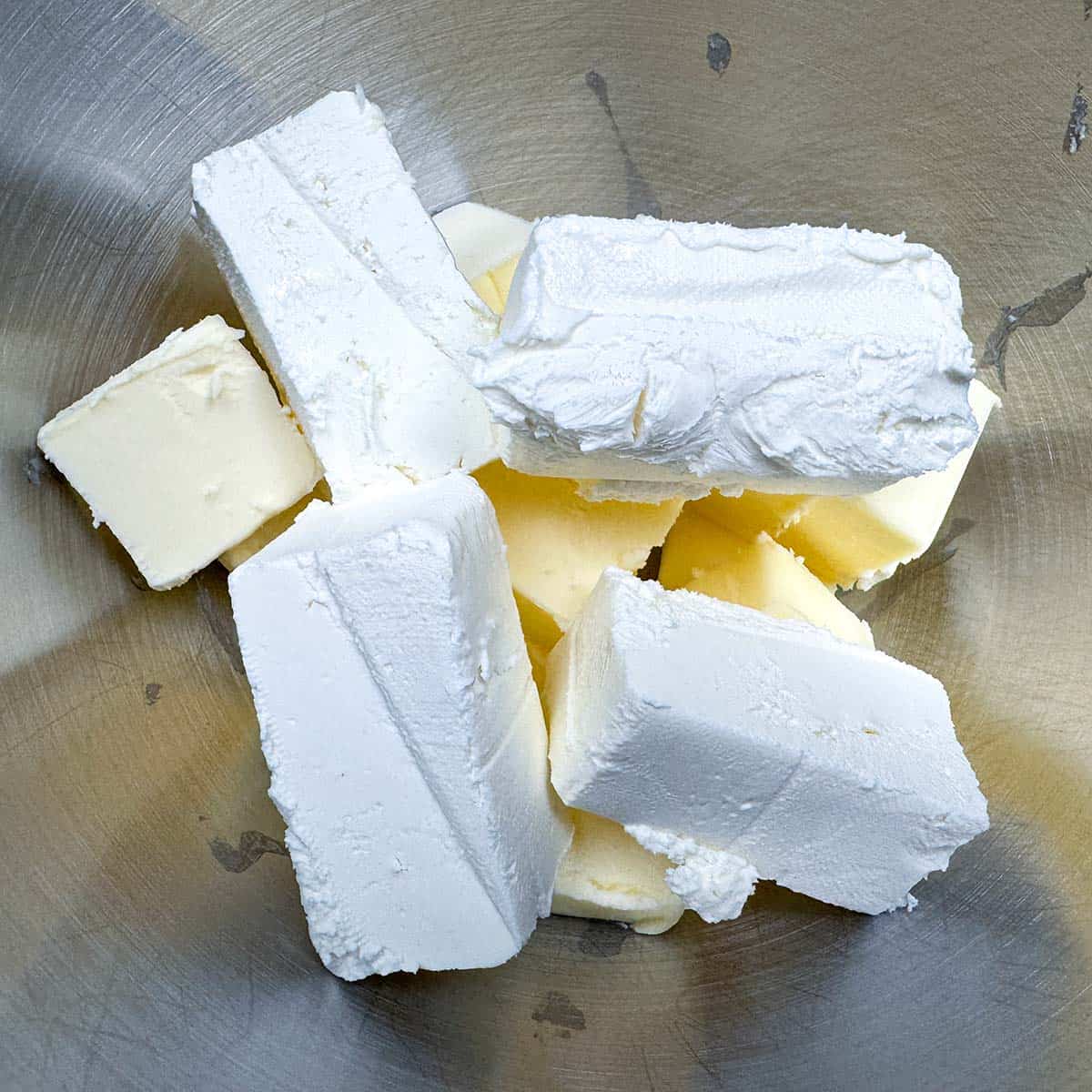 Cubed butter and blocks of cream cheese in a mixer bowl.