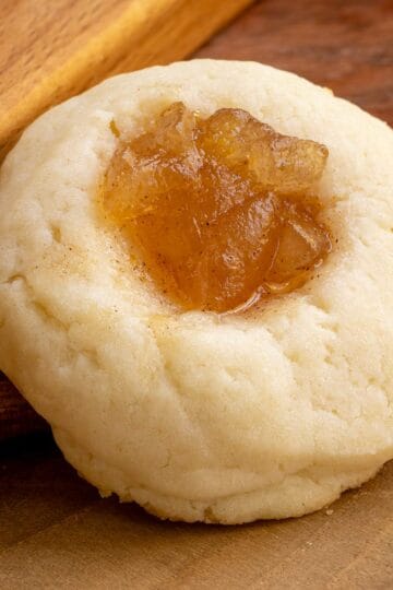 A thumbprint cookie with pear filling on a wooden board.
