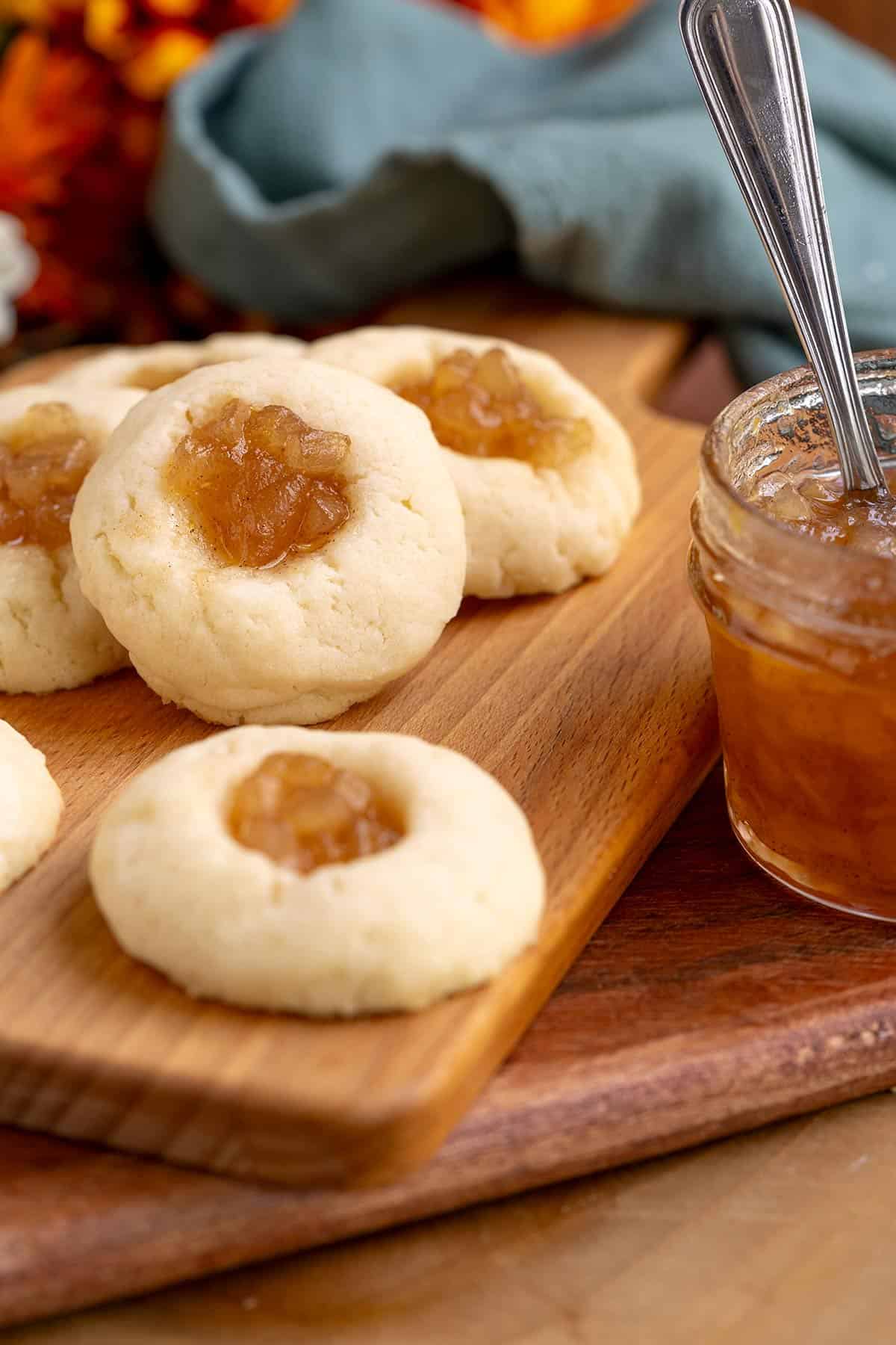 Thumbprint cookies with pear filling on a wooden cutting board with a jar of the pear filling beside them.