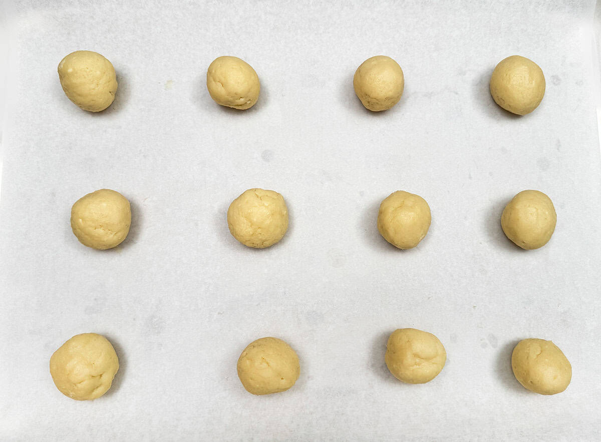 Twelve cookie balls on a parchment-lined sheet pan.