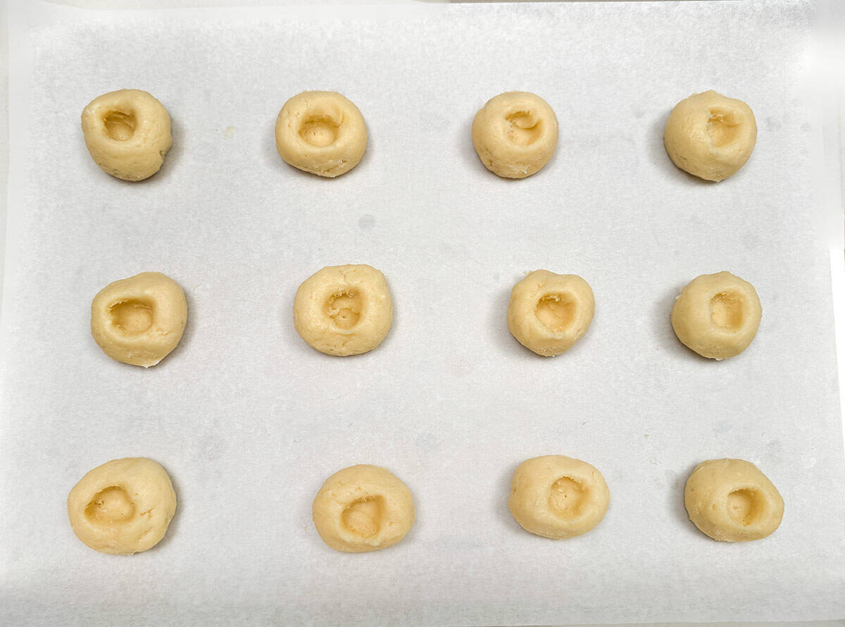 Twelve cookie dough balls have wells pressed into their centers for pear filling.