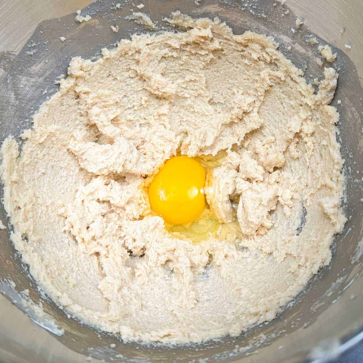 In a mixer bowl adding an egg to the butter-sugar mixture.
