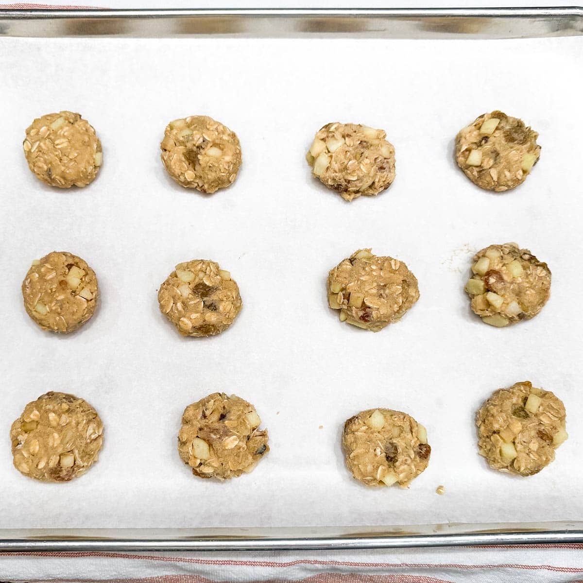 Twelve flattened scoops of cookie dough on a parchment paper lined sheet pan.